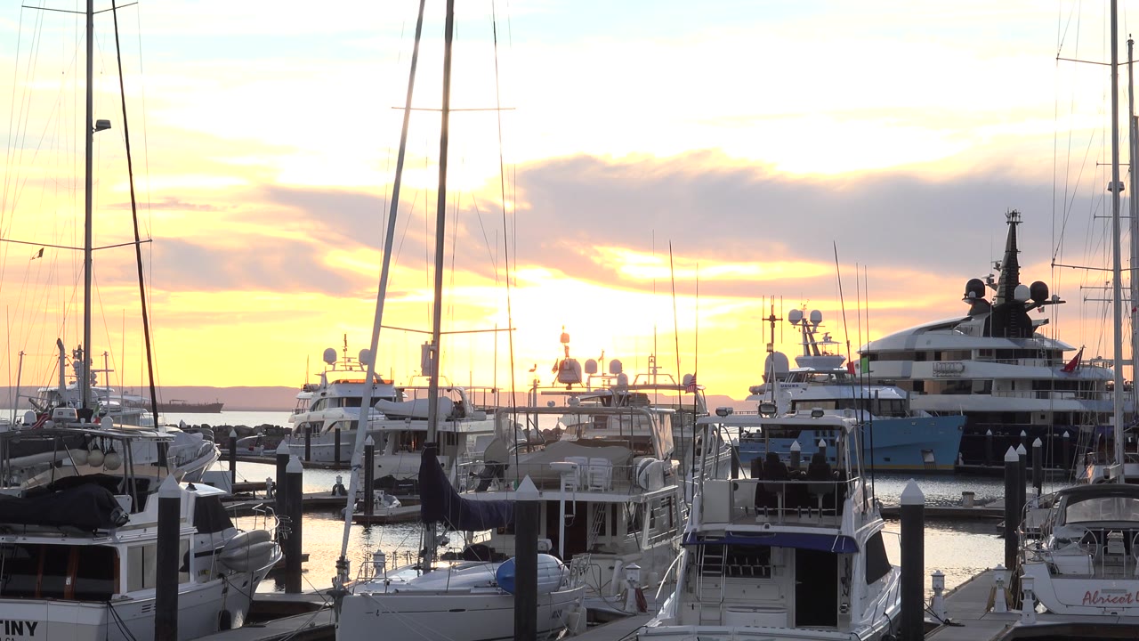 Docked boats and yachts in a marina at sunset.