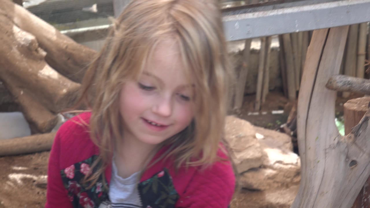 The girl looks down in Cabo San Lucas, Mexico, with her face close to camera and the wood-and-rock enclosure background filling the frame.