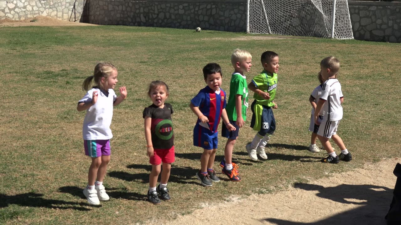 Children in sports clothing jumping on a grass field.