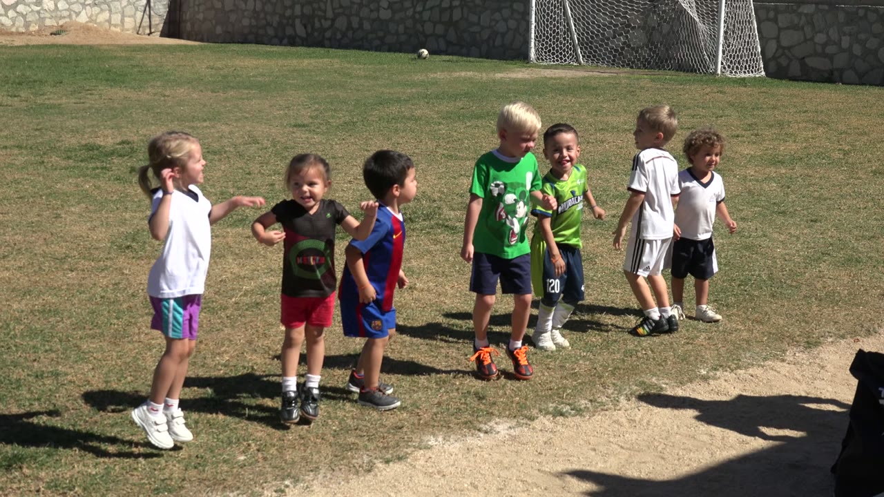 Children standing on a sunlit soccer field near a goal.
