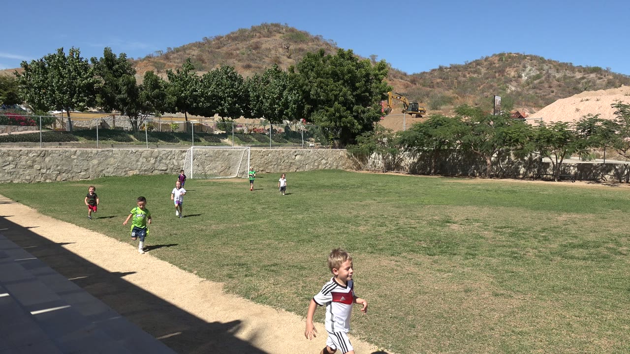 Children running on a grass soccer field near a sideline path.