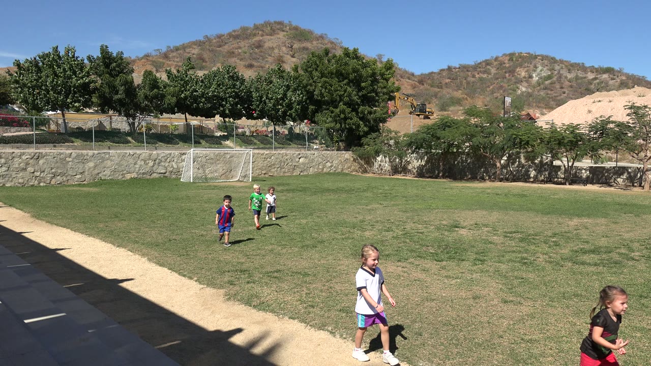 Two children pass near the camera while others remain farther back on the field.