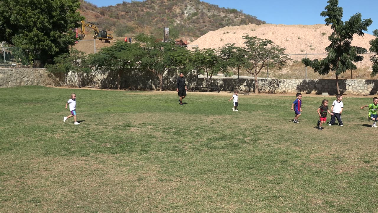 Children running across a grassy field with an adult in the background.