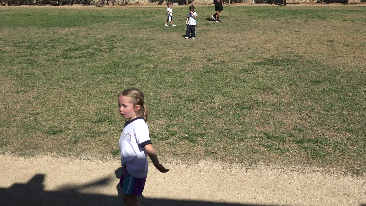 Girl standing near a sandy border beside the grassy field.