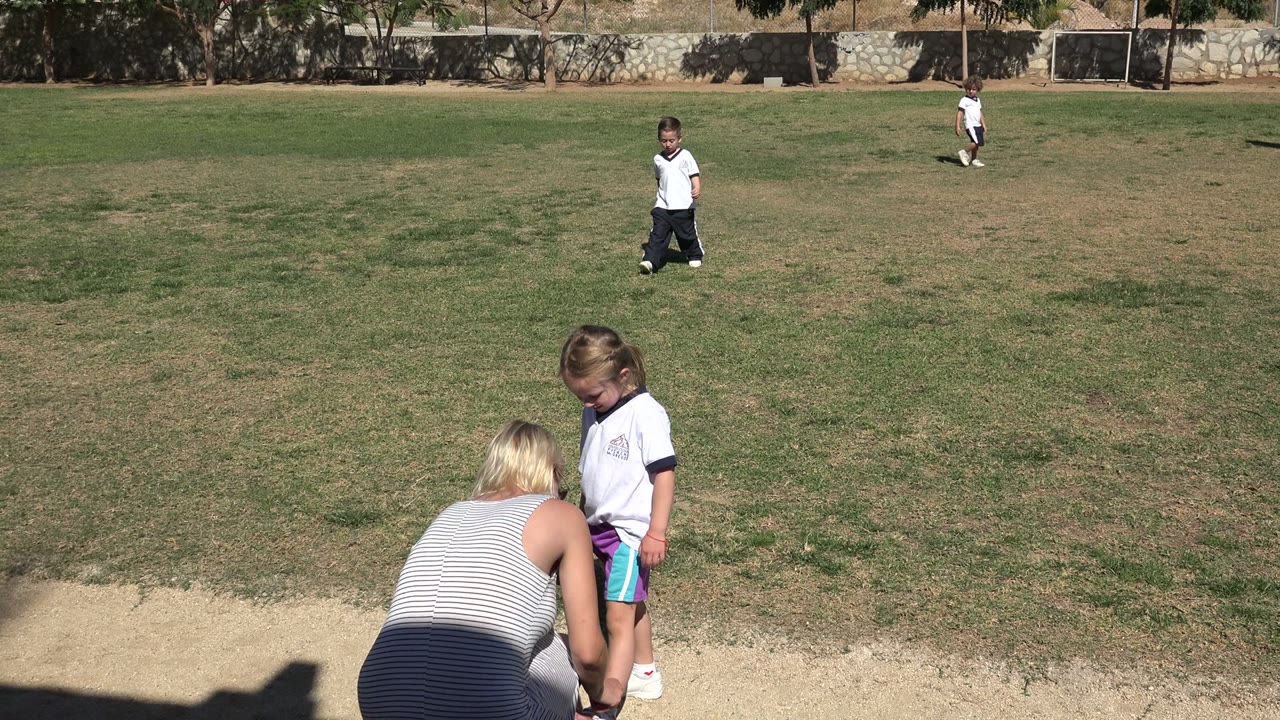 Woman crouching by a young girl on grass near a dirt path.