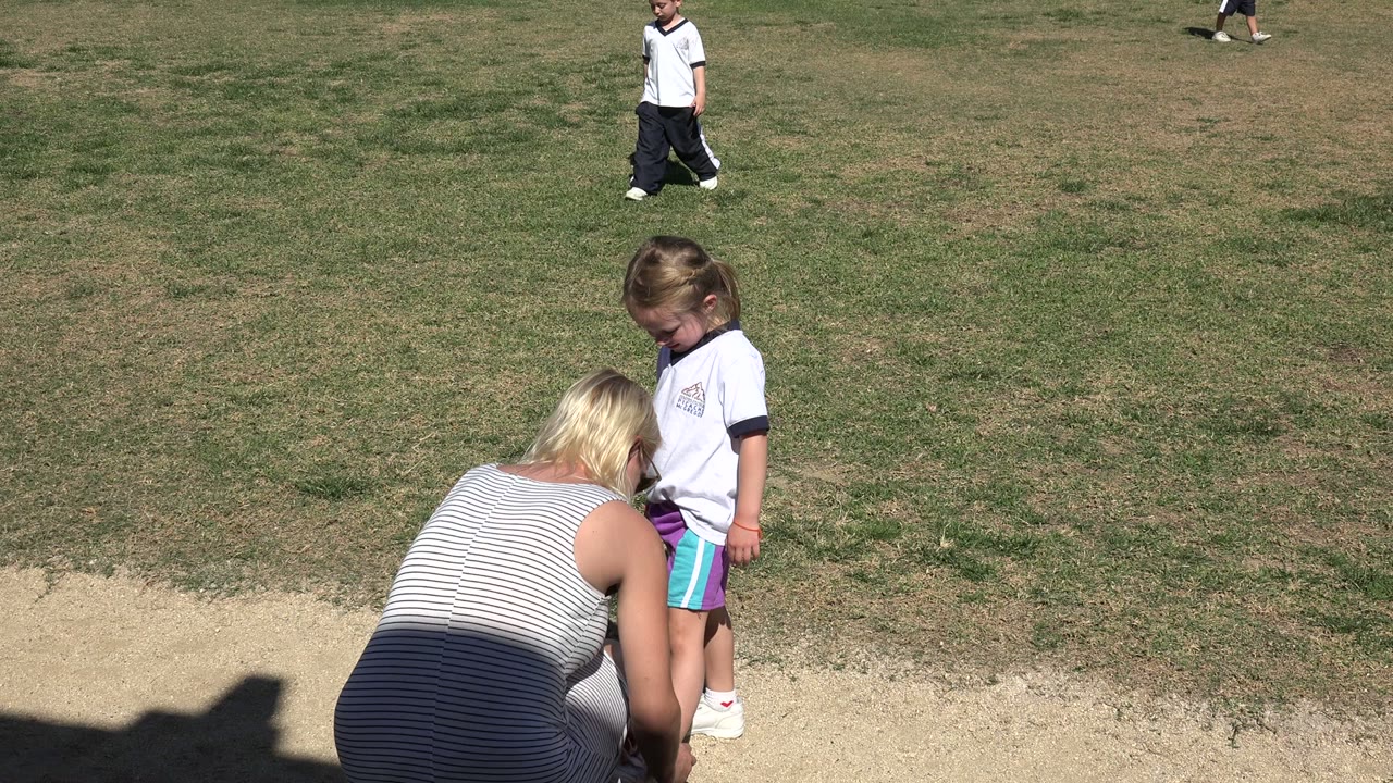 In Los Cabos, Mexico, the woman remains crouched with her back to camera while the young girl looks down toward her shoes on the edge of the grass.