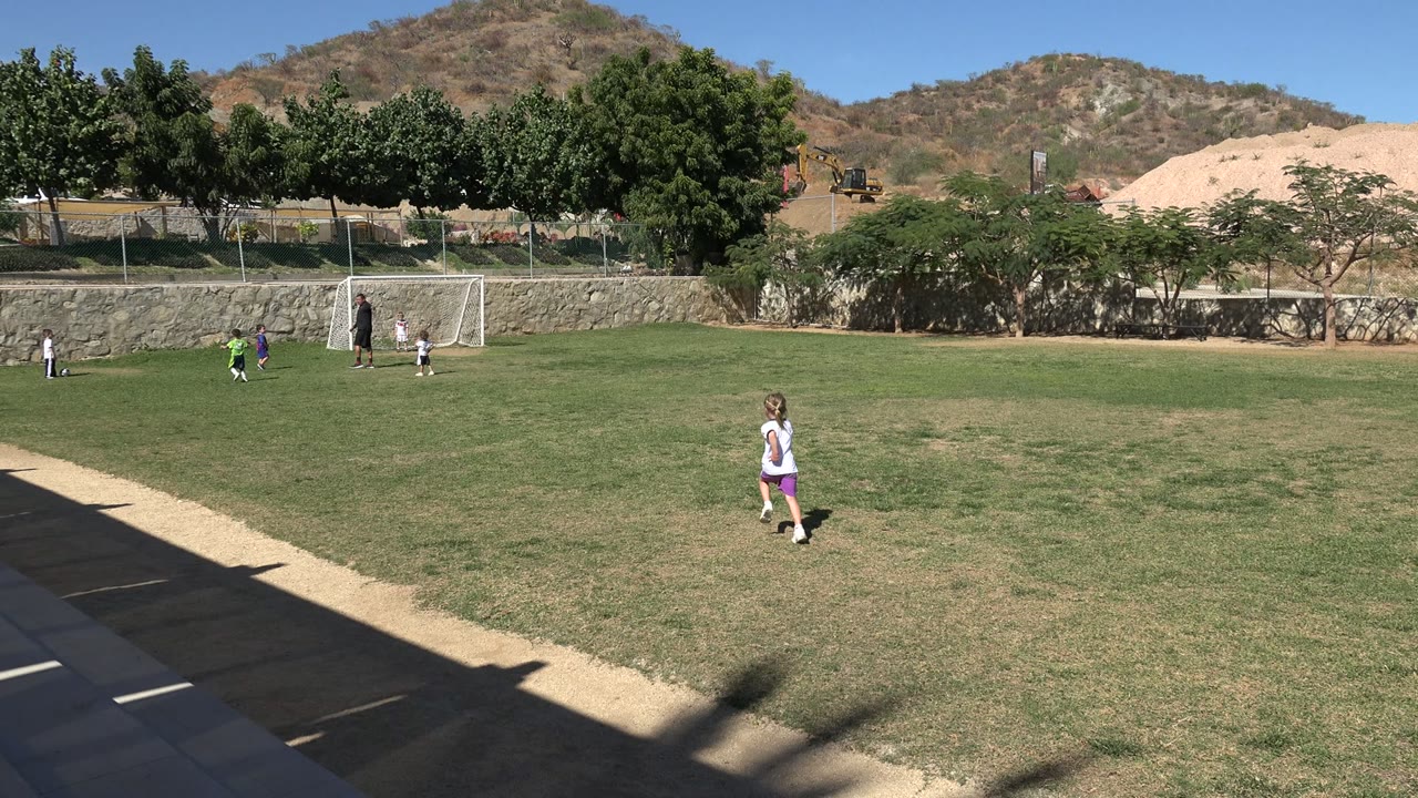 Child running on a soccer field with other kids near a small goal.