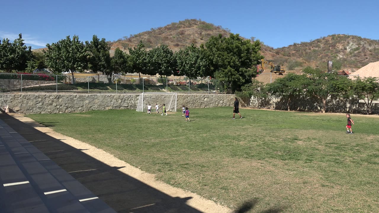 Wide soccer field with children near a small goal and an adult teacher nearby