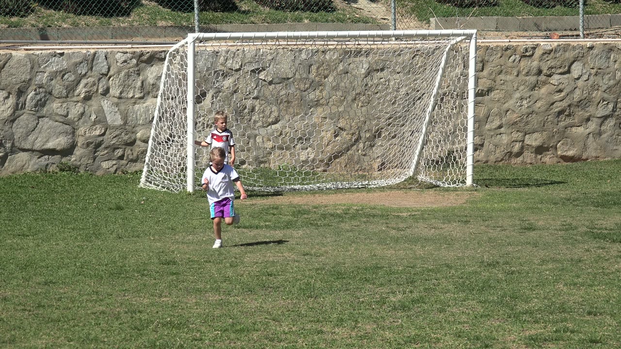 Young child running on a soccer field with a goal behind them.