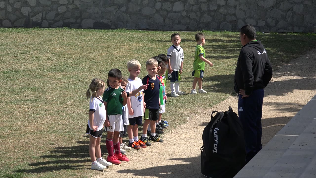 Children in soccer uniforms line up while a coach stands nearby.