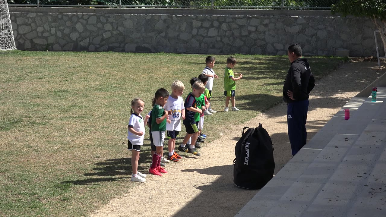 Children line up on a grass field beside an adult instructor.