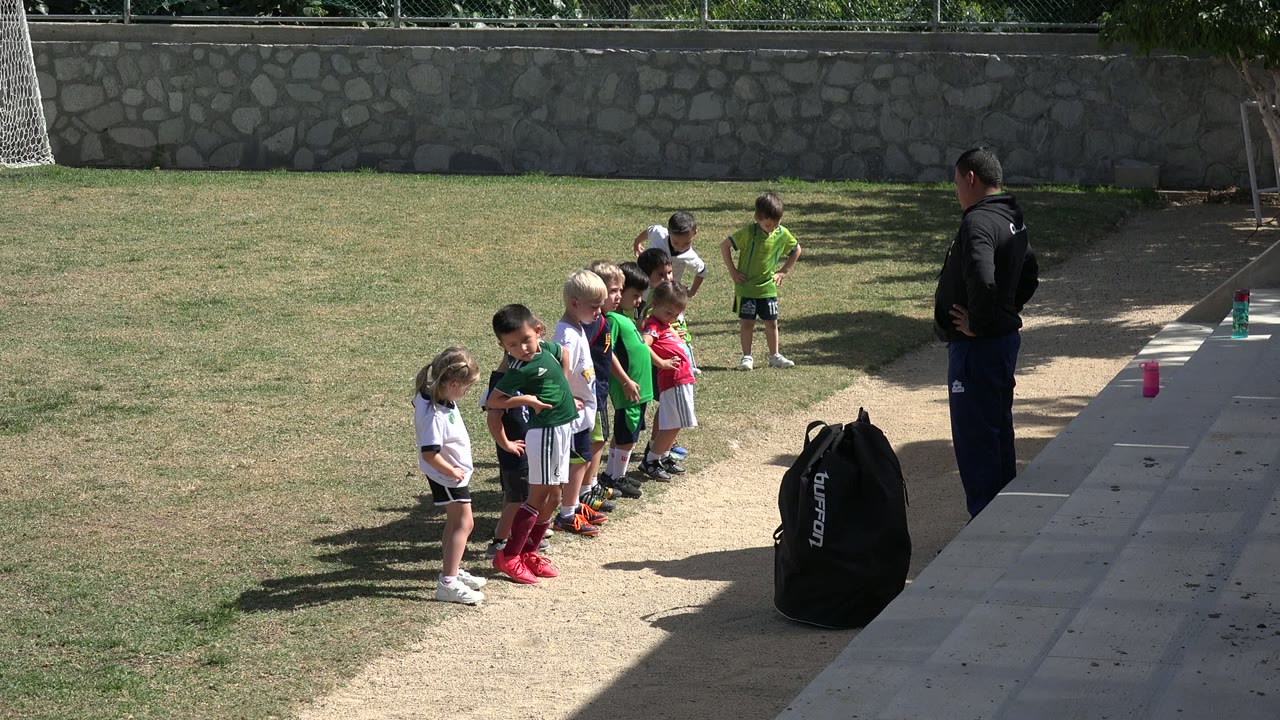 Children in sports clothes stand together with a coach near the sideline.
