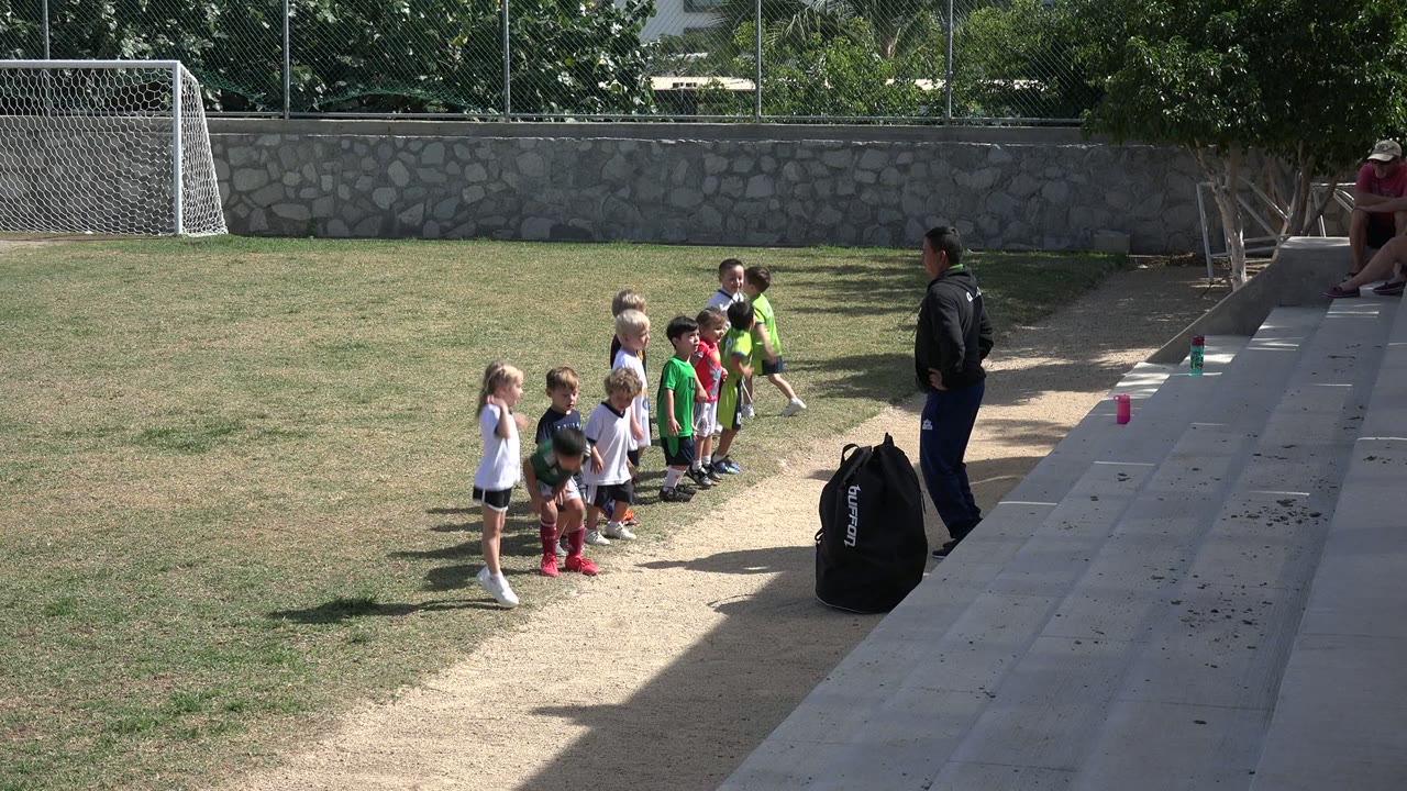 Children lined up on grass facing an instructor near concrete steps.