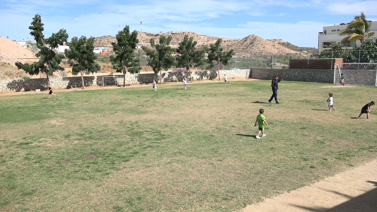 Adult and children on a sunlit football field near small goals.
