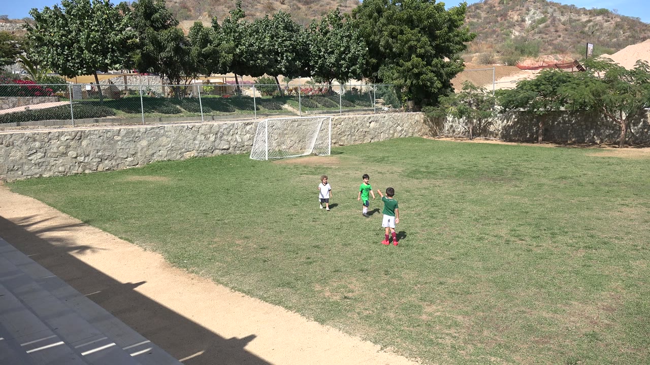 Three children standing on a soccer field near a small goal.