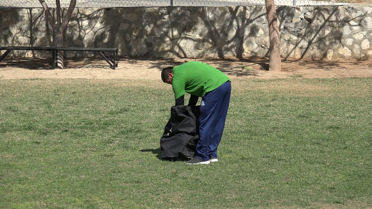 Man bending over a black bag on a grassy field.