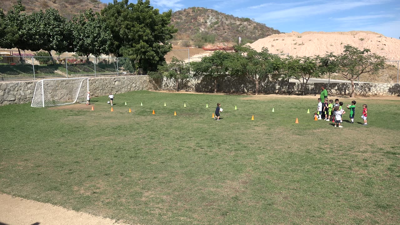 Children and a coach gather near cones on a soccer field.