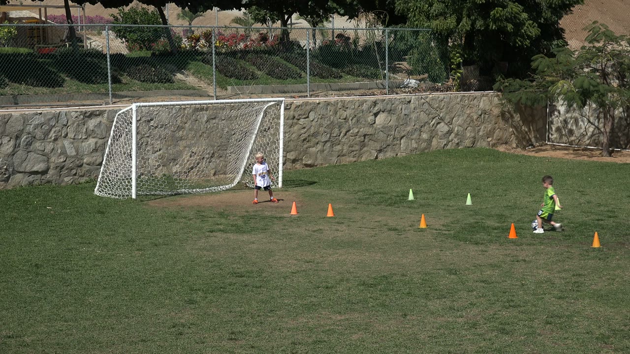 Child in green shirt approaches the soccer ball near training cones.