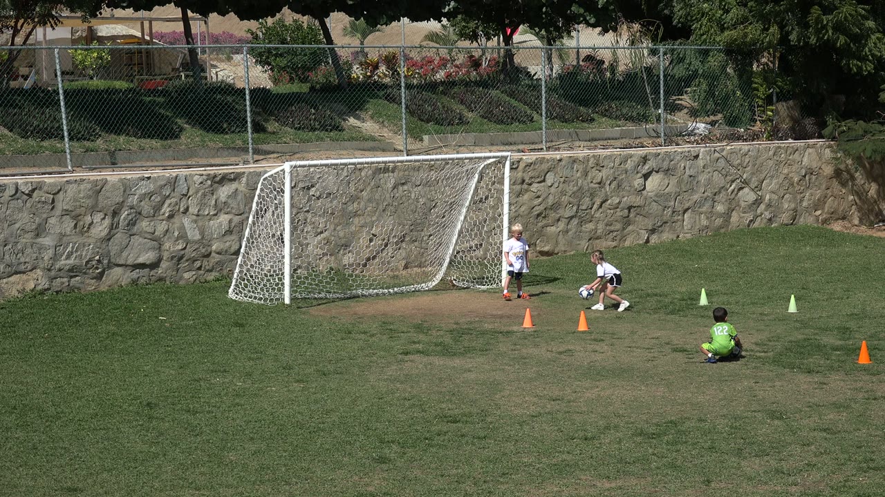 Children near a football goal with one child seated on the grass.