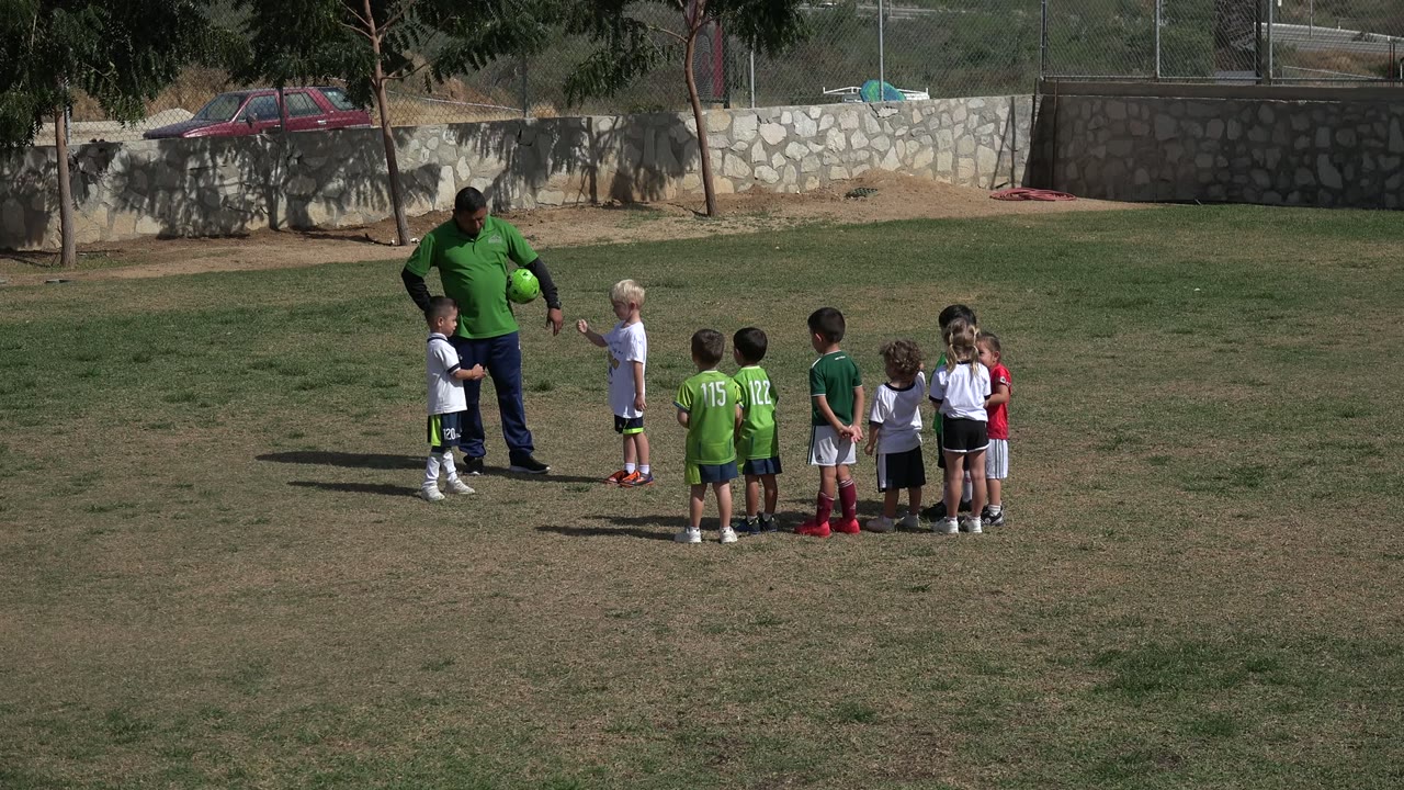 Adult and children gathered on a grass soccer field.