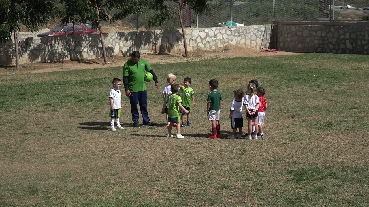 Man in green shirt holding a ball near children on a grass field.