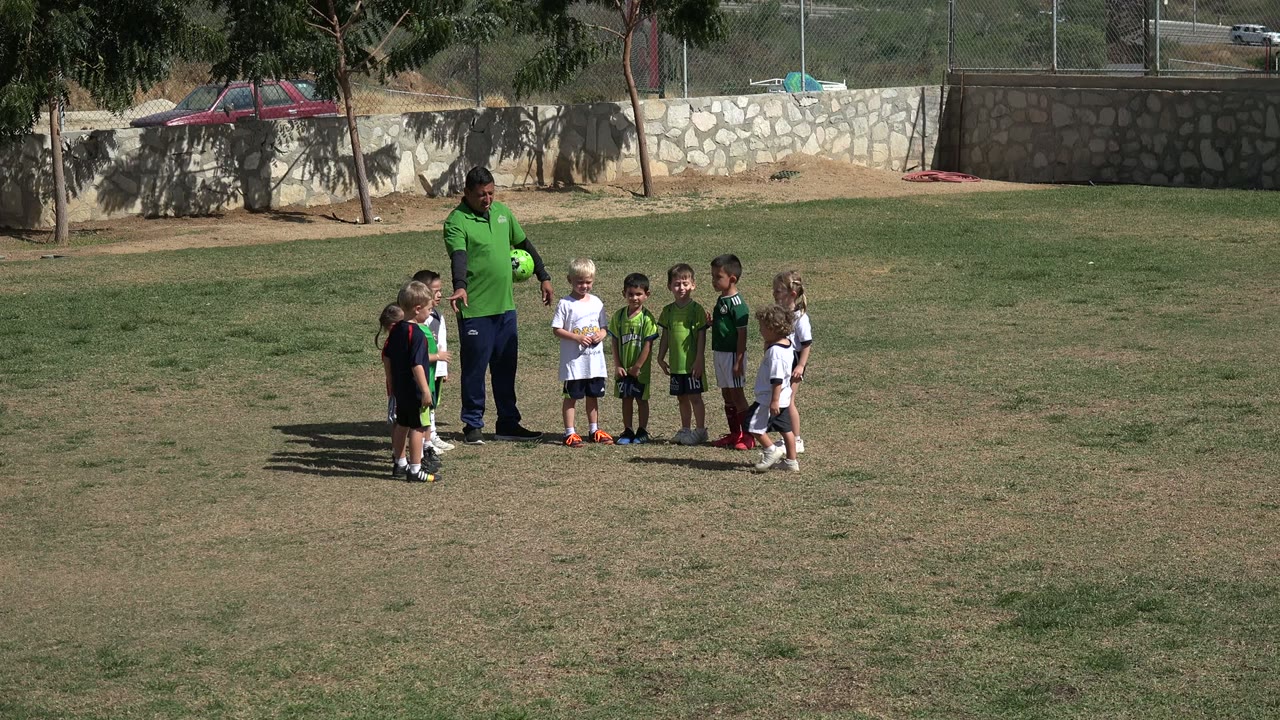 Coach and children stand in a loose circle on the field.