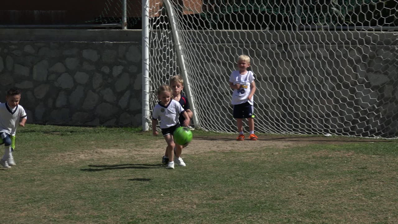 Children run near a green soccer ball in front of a goal net.