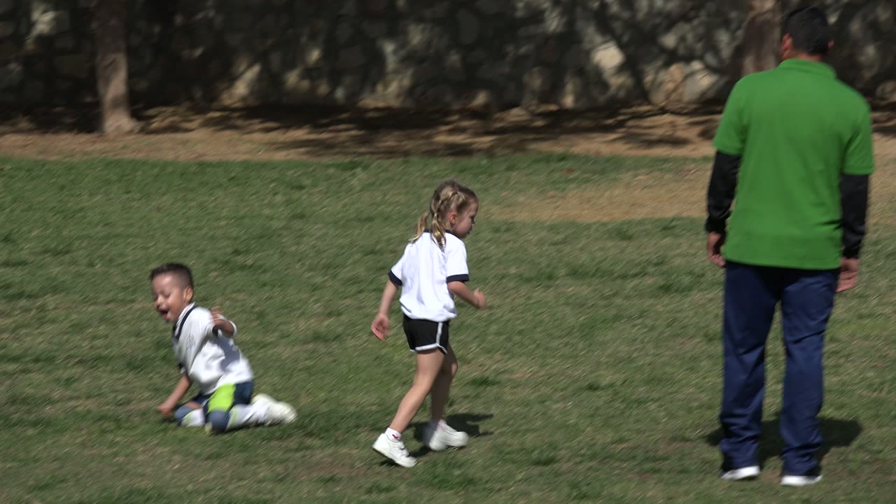 In Los Cabos, Mexico, a boy is down on the grass as a girl in a white shirt runs nearby on the open field.