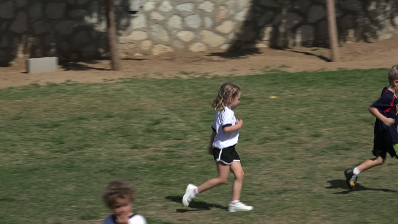 Girl and boy running across a grassy soccer field