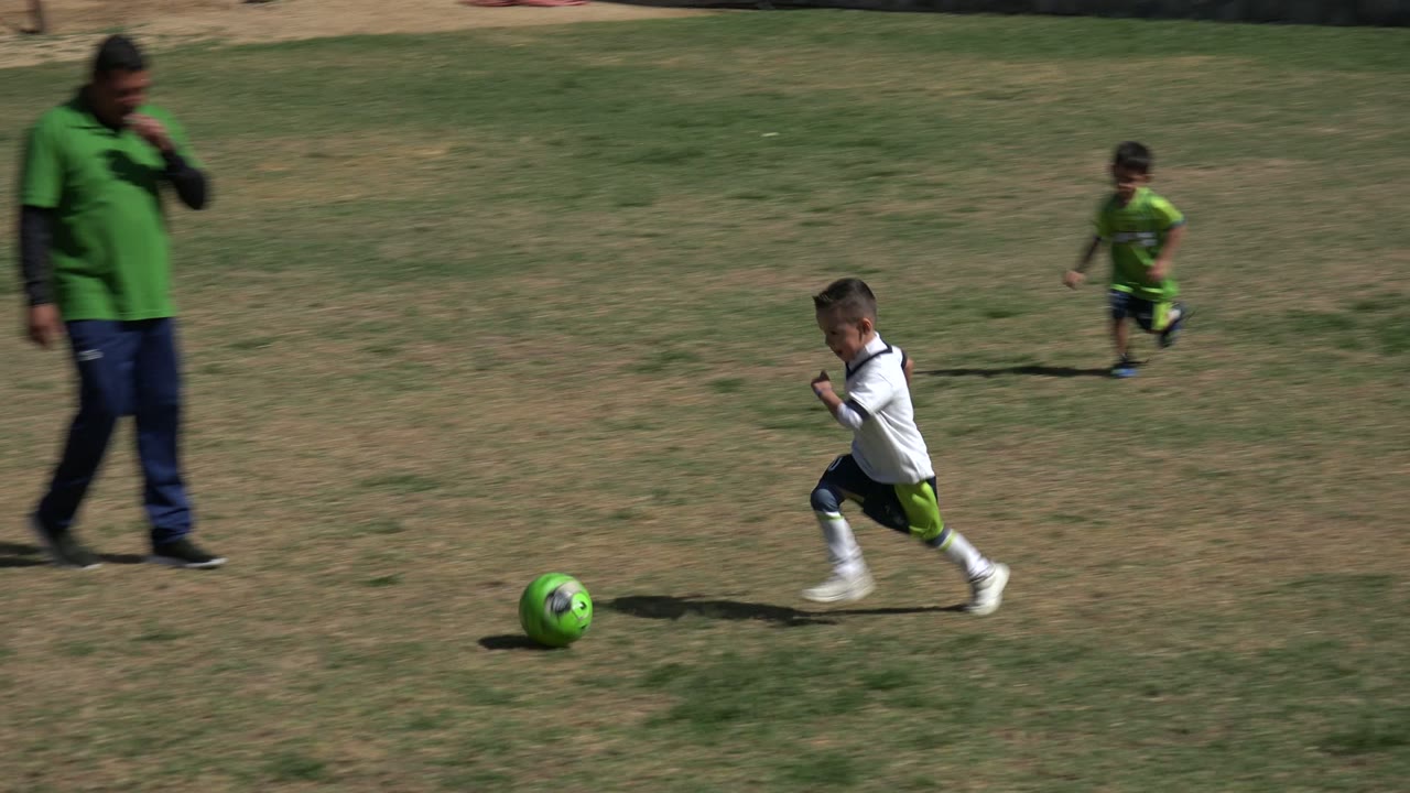 Boy running after a green soccer ball across open patchy grass.