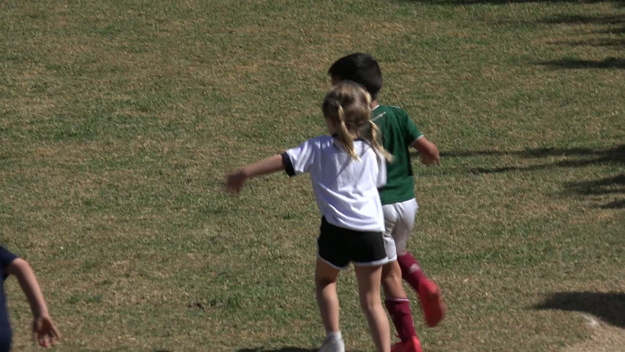 Two children run across a sunlit grass soccer field.
