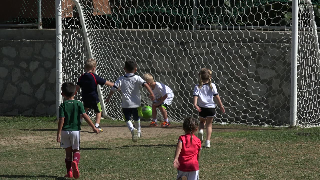 A group of children crowd the goal area in Los Cabos, Mexico, as a player in white bends near the ball by the net.