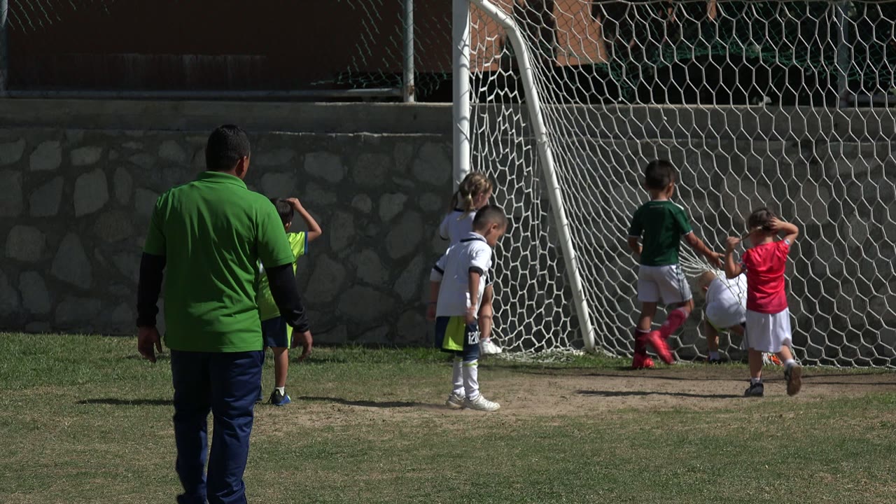 Children stand beside the soccer goal while the coach nears them.