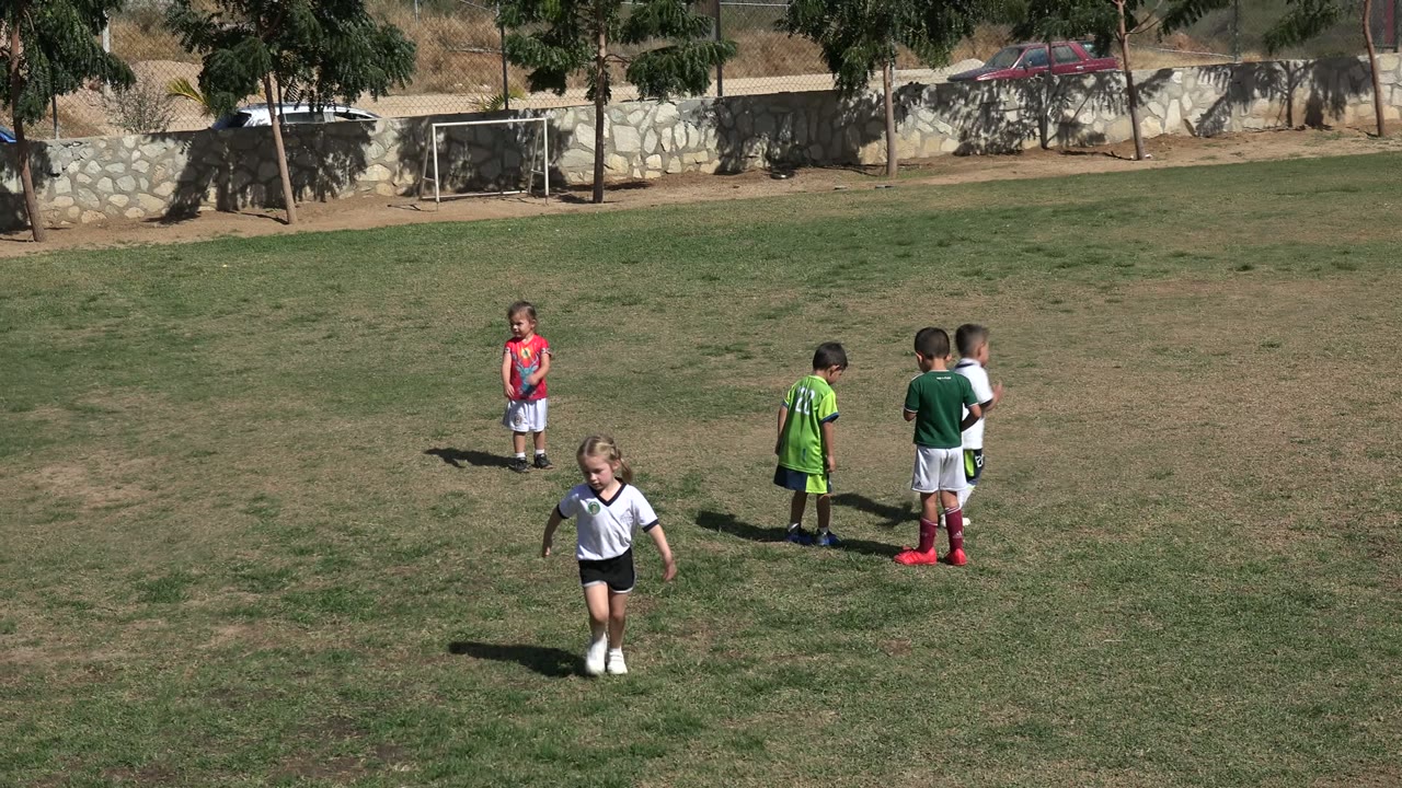Children on a dry grass football field with small goals in the background.