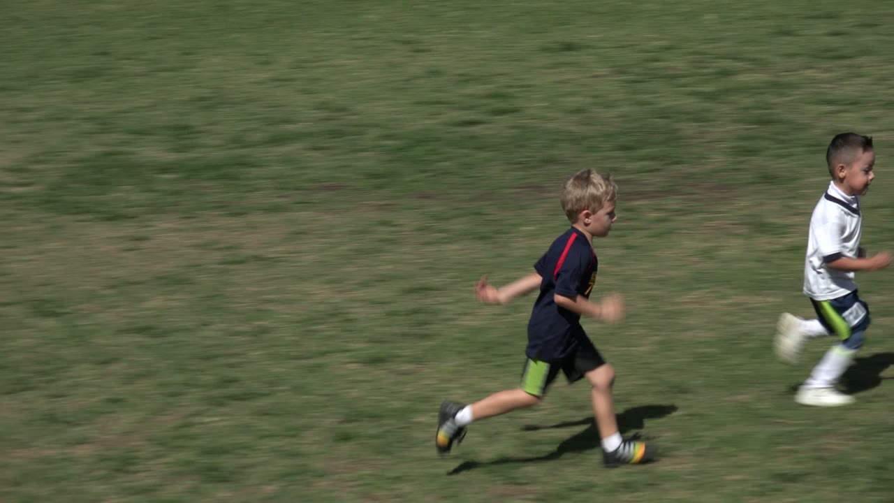 Two boys running across grass during a football game.