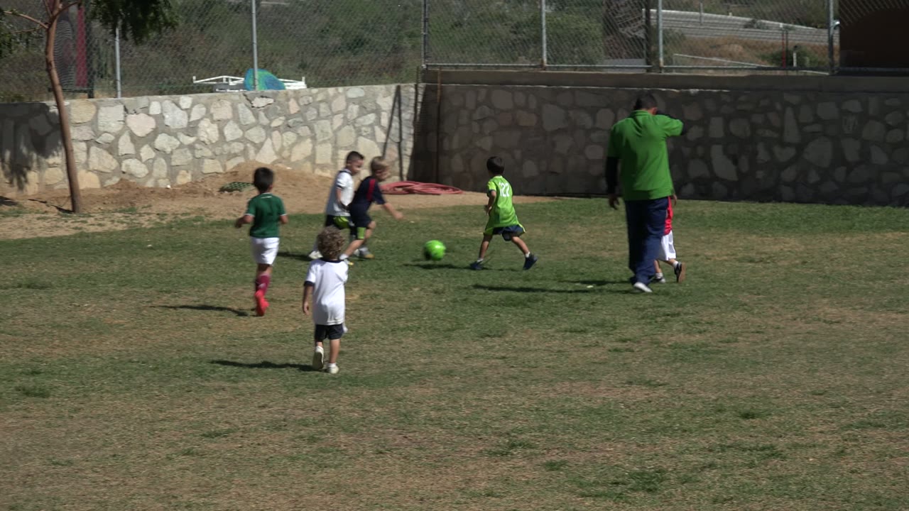 Young players run across the field as the coach stands to the right.
