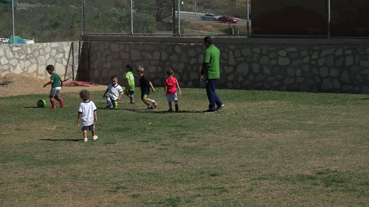 Children and an adult on a soccer field near a stone wall.