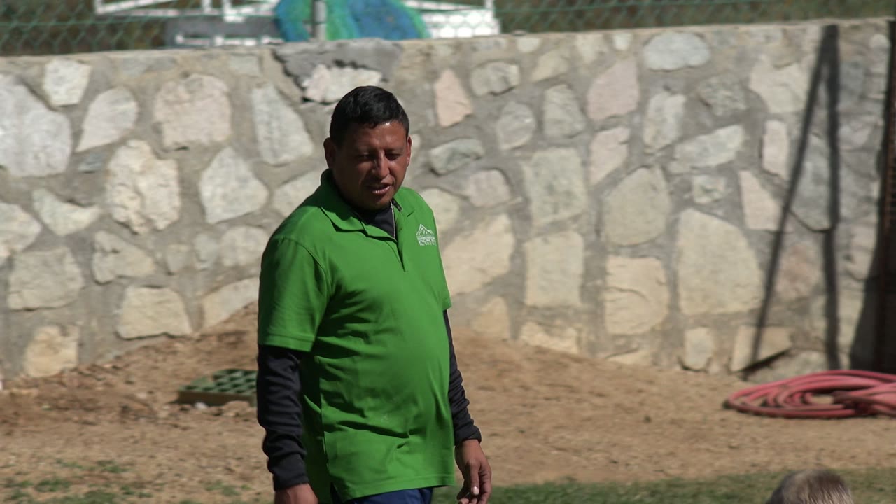 The man faces forward on the grass in Los Cabos, Mexico, with the stone wall filling the background.