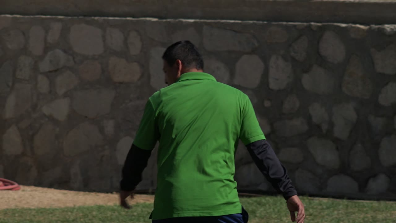 Man in green shirt walking beside a stone wall.