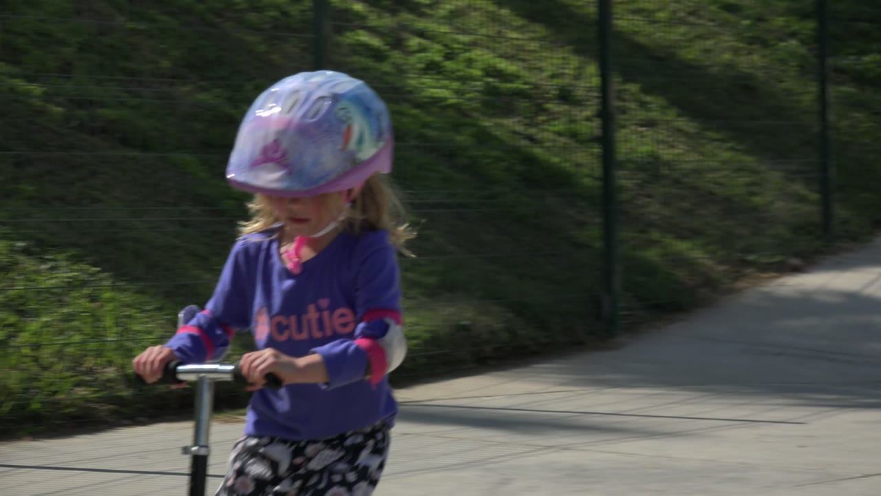 Young girl in a helmet riding a scooter on a paved path.