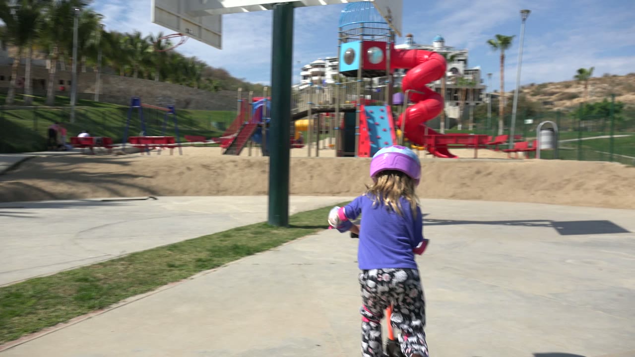 Child on scooter approaching an open playground court.