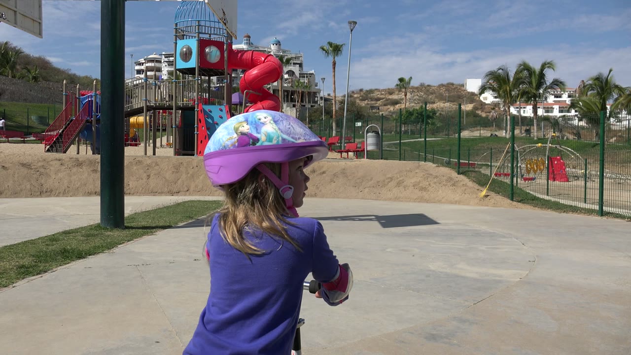 Child in a helmet at a sunny playground with red slides.