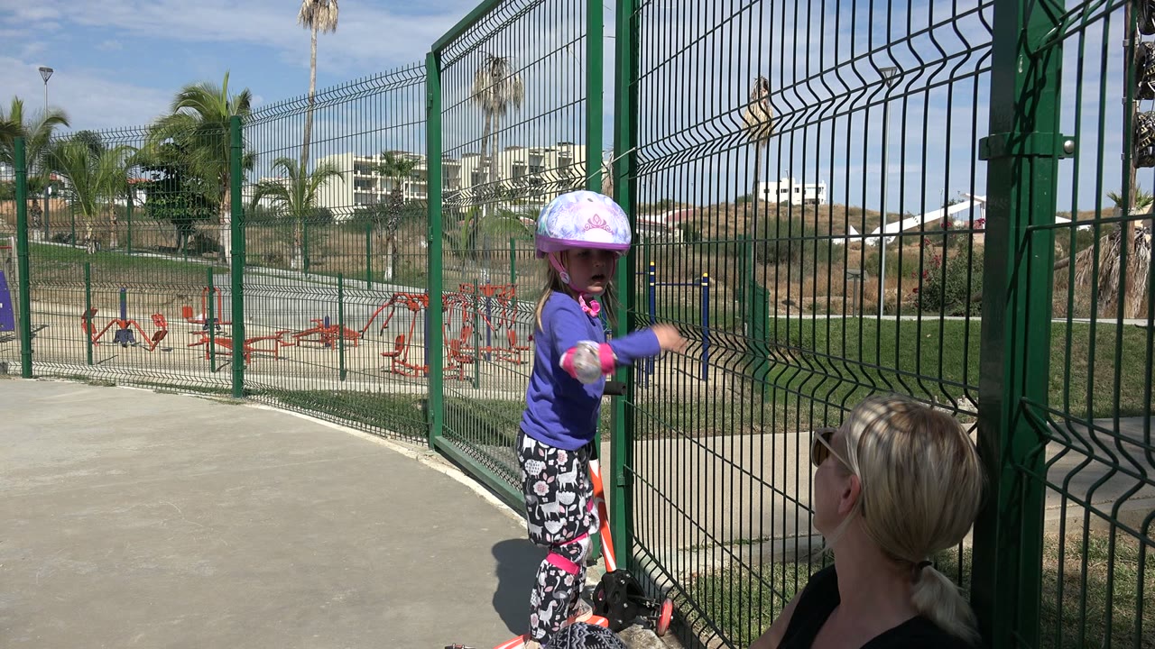 Girl stands near the fence and looks back toward the adult woman.