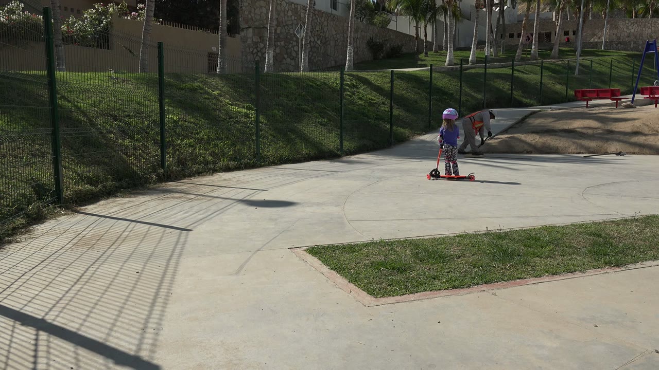 Child on scooter with worker near fenced play area