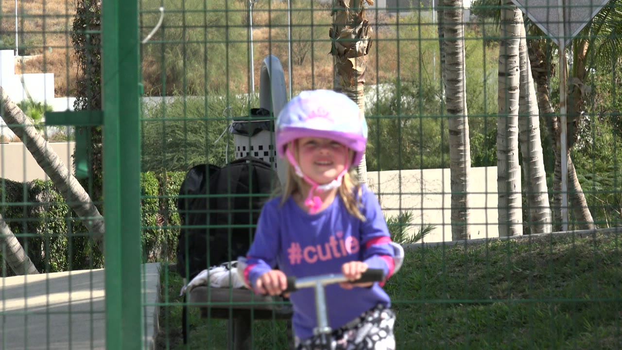 The young blonde girl faces camera more clearly while holding scooter handlebars in the sunny Los Cabos outdoor setting.