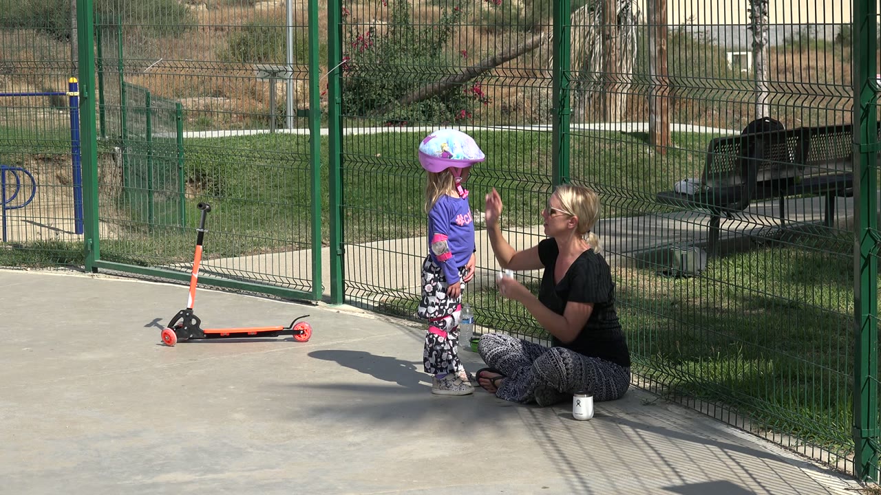 Woman kneeling beside a helmeted child near a scooter