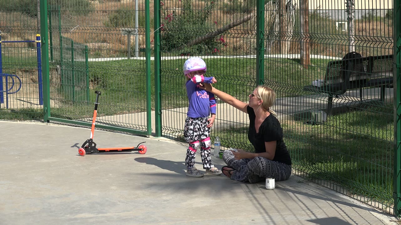 Girl in a helmet stands by a scooter while a woman reaches toward her face.