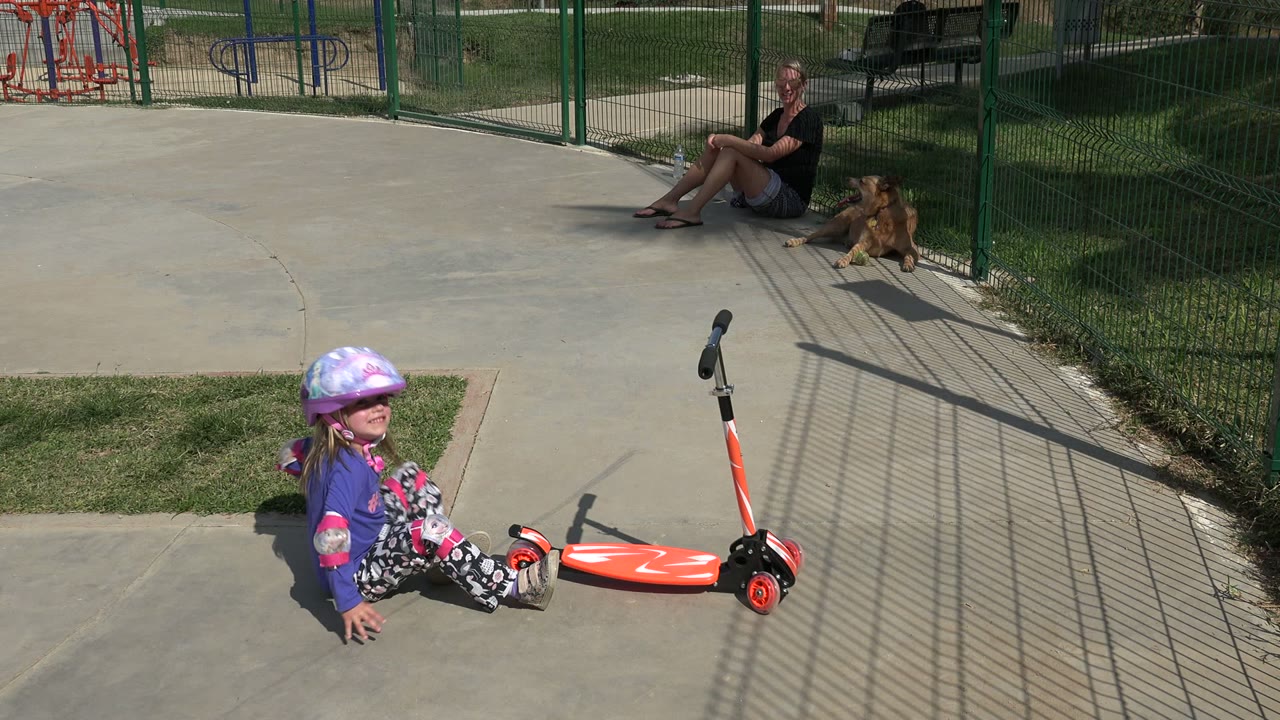 Girl smiles while seated near an upright red scooter.