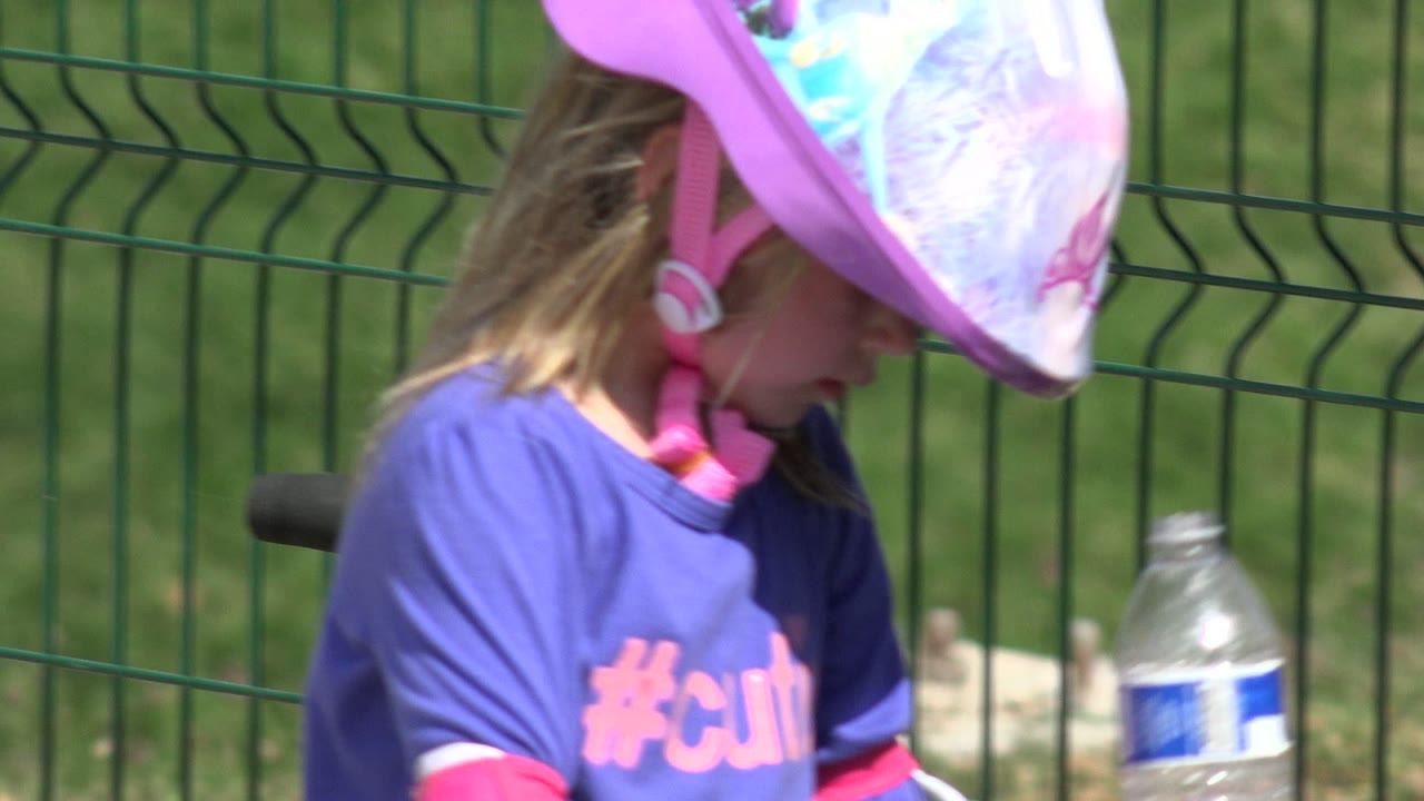 Child in a pink helmet looks downward near a scooter and a plastic water bottle.