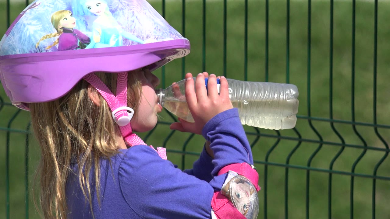 The child remains in side profile in Los Cabos, Mexico, holding the bottle with both hands while the purple helmet and pink strap fill the top of the frame.